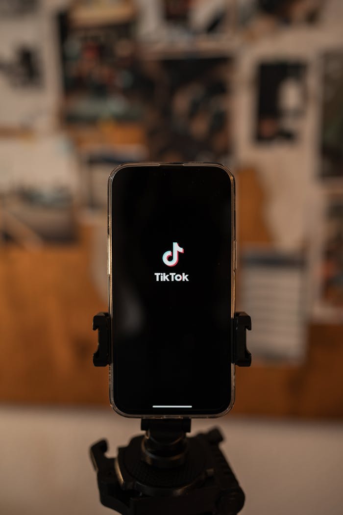 services-08 Close-up of a smartphone on a tripod displaying the TikTok app. Blurred background.