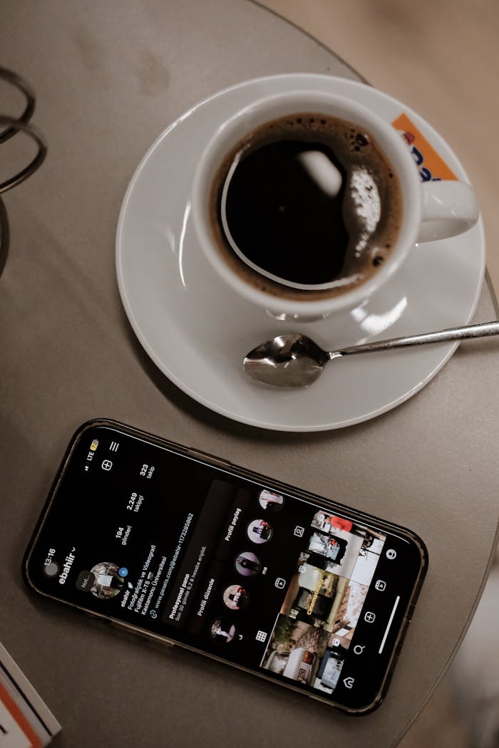 services-header A cup of black coffee next to a smartphone displaying a social media app on a cafe table.