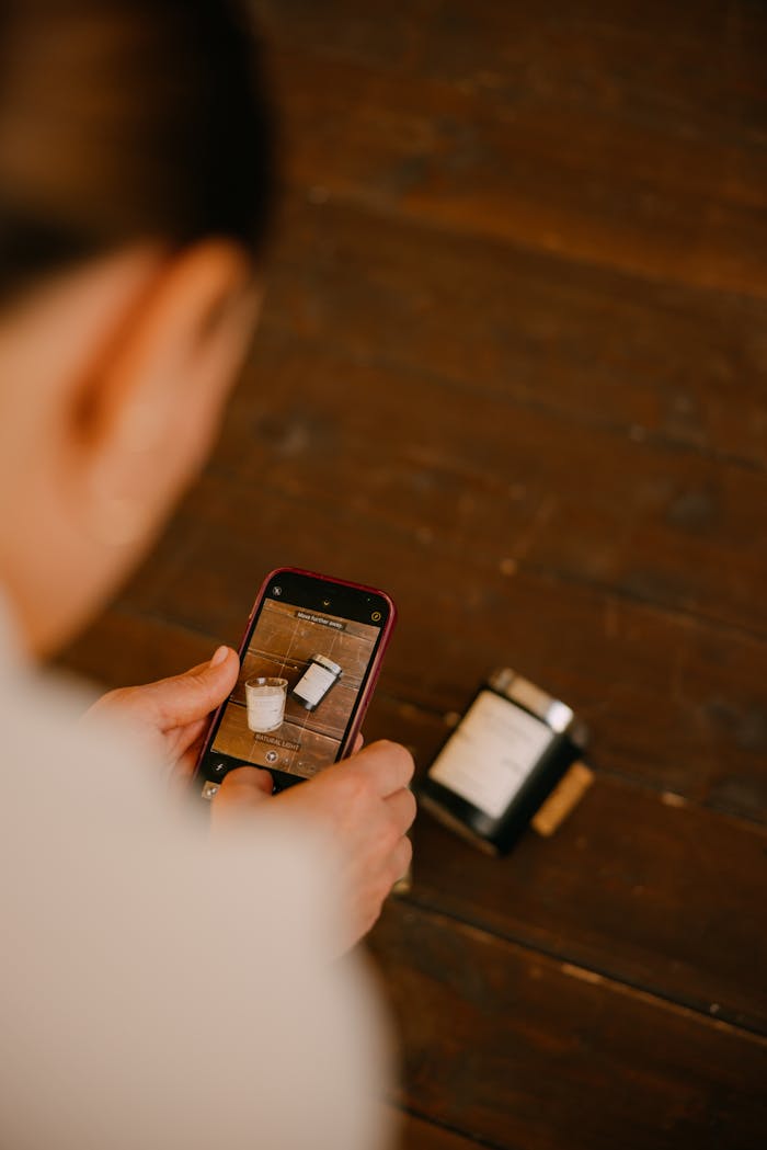 A person photographing a minimalist coffee and candle setup on a wooden table.